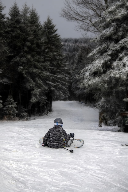 Free photo vertical shot of a person sitting on the hill wearing snowboard