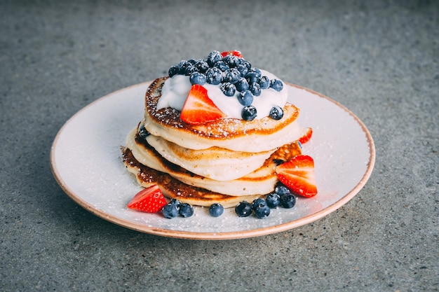 Vertical shot of a plate with gourmet pancakes with cream strawberries and blueberries