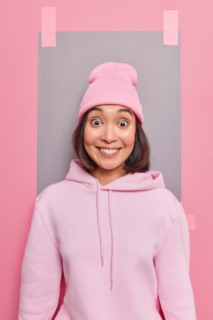 Vertical shot of positive good looking Asian girl smiles happily hears excellent news wears casual clothes has fascinated expression poses against blank copy space checks out something awesome