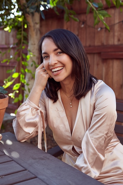 Vertical shot of a pretty female with a pink silk dress sitting in an outdoor cafe