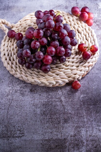 Vertical shot of red grapes on a round board on a gray surface