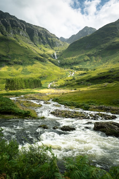 Free photo vertical shot of a river surrounded by the mountains and meadows in scotland