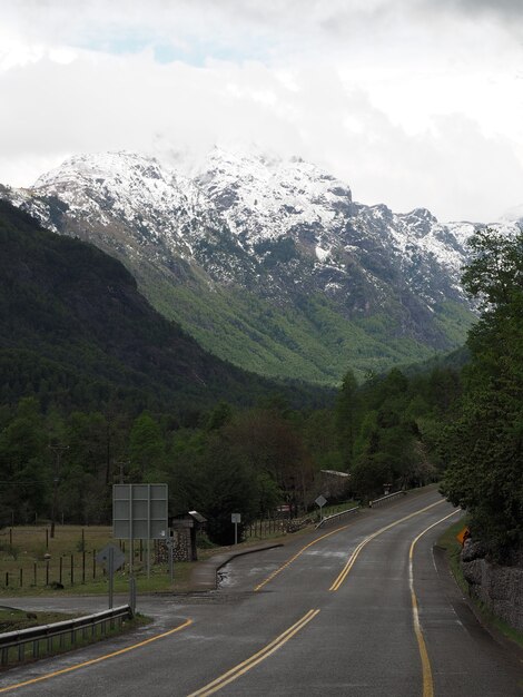 Vertical shot of a road and tree-covered mountains with snowy peaks