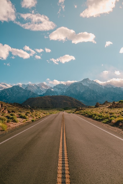 Vertical shot of a road with the magnificent mountains under the blue sky captured in California