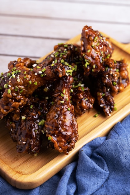 Free photo vertical shot of roasted chicken pieces on a wooden plate and some seasoning on it