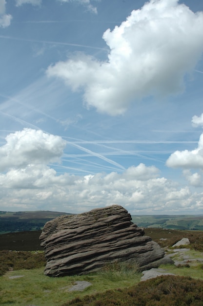 Free photo vertical shot of a rock on a grass under a blue sky with clouds