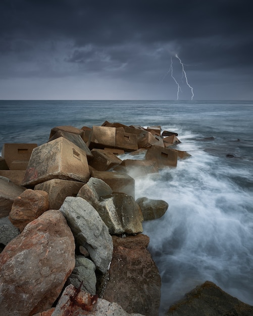 Free Photo vertical shot of rocks in the sea during a thunderstorm and lightning