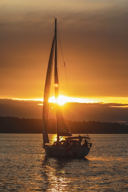 Free Photo vertical shot of a sailing boat in the ocean during sunset