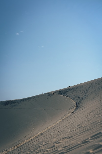 Free photo vertical shot of a sand dune with people walking in the distance and a clear blue sky