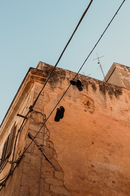 Free Photo vertical shot of shoes handing from an electric cable near a building under a blue sky