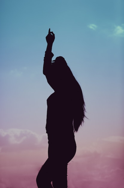 Free photo vertical shot of a silhouette of a female dancing during a beautiful sunset