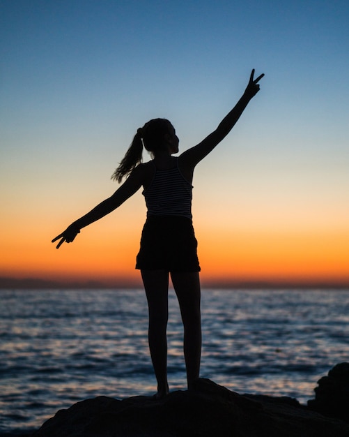 Vertical shot of the silhouette of a female with her arms open showing the victory sign