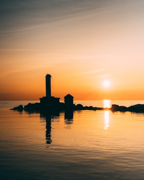 Vertical shot of silhouettes of the buildings in the middle of a calm ocean during sunset