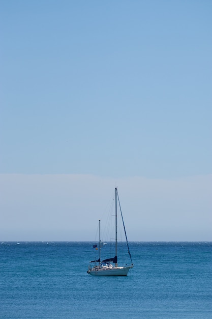 Free Photo vertical shot of a small boat sailing in the ocean with a clear blue sky