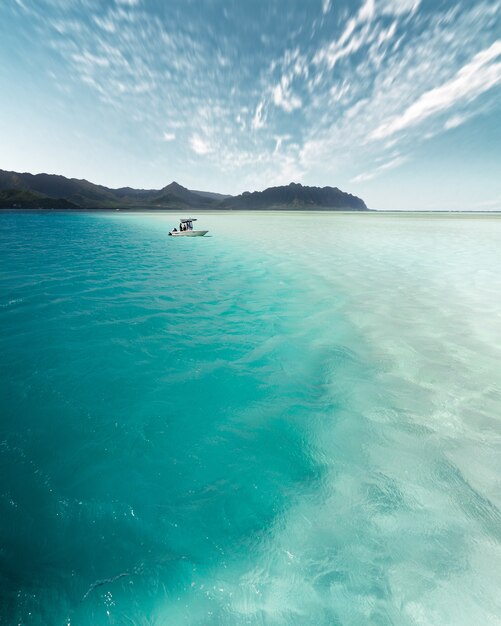 Vertical shot of a small boat travelling across the beautiful ocean during daytime