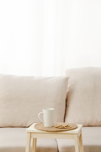 Vertical shot of a small table with a mug on it near a beige sofa under the lights