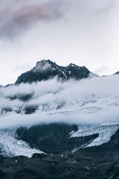 Vertical shot of a snowy mountain top above the clouds with a clear sky