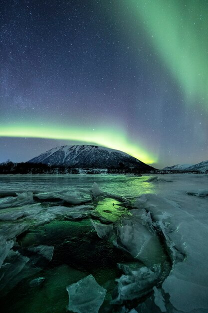 A vertical shot of snowy mountains under a polar light