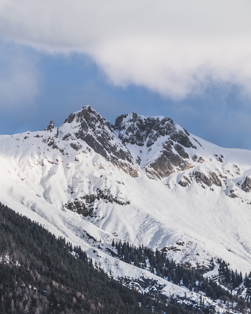 Vertical shot of the snowy peaks of the mountains under the cloudy sky