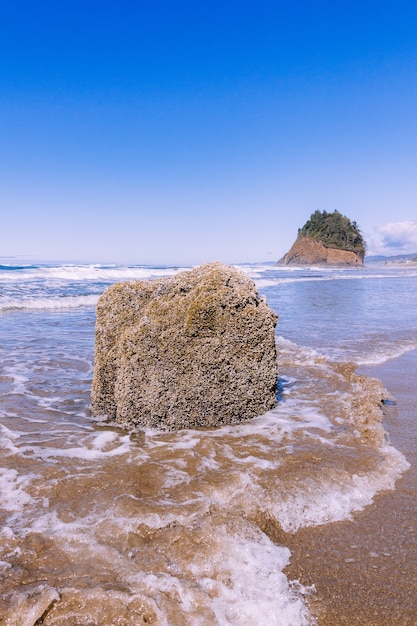 Vertical shot of a stone in the ocean under the blue clear sky