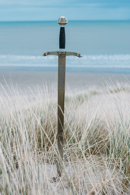 Free Photo vertical shot of a sword in the beach during daytime