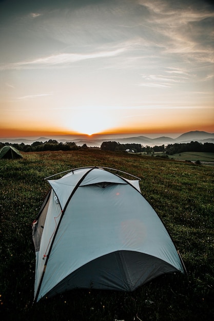 Vertical shot of a tent on a hill covered in greenery during a beautiful sunrise in the morning