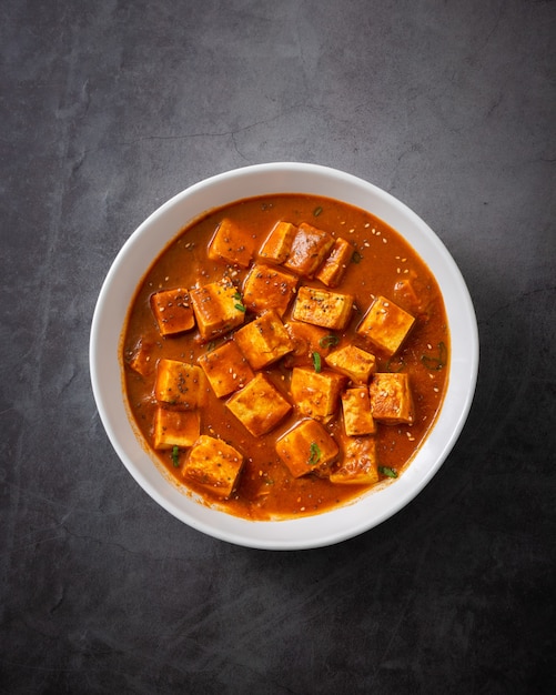 Free photo vertical shot of traditional indian paneer butter masala or cheese cottage curry on a black surface