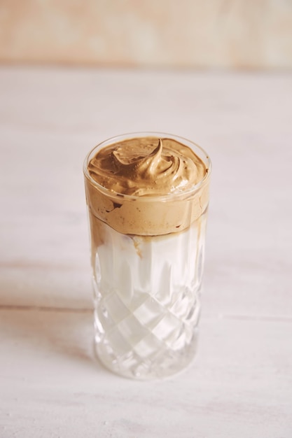 Free photo vertical shot of a trendy delicious fresh dalgona coffee with milk on a white wood table