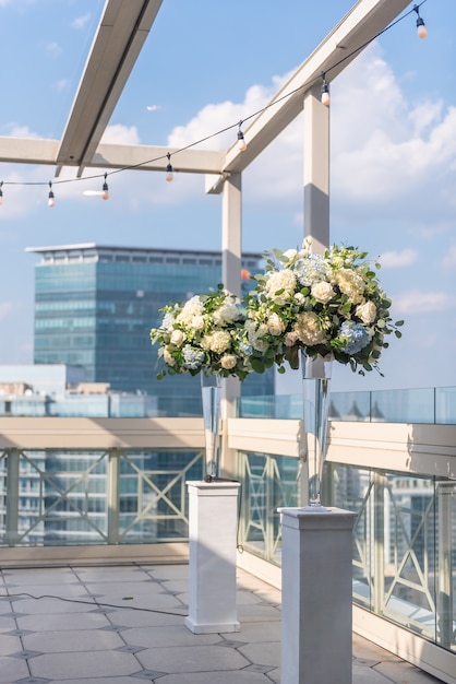 Vertical shot of two vases with beautiful flowers on whit columns on the roof of a building