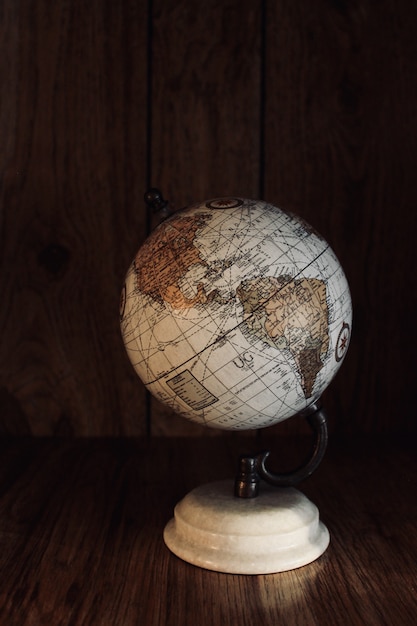 Free Photo vertical shot of a vintage globe model on a wooden table with a wooden wall in the background