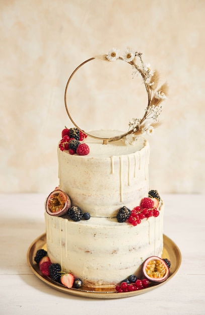 Free photo vertical shot of a wedding cake decorated with fresh fruits and berries and a flower ring