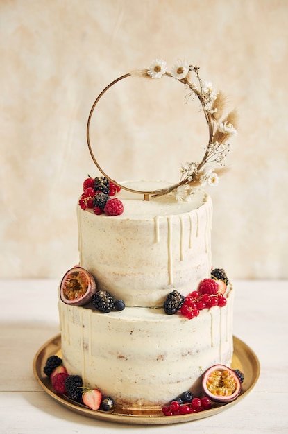 Free photo vertical shot of a wedding cake decorated with fresh fruits and berries and a flower ring