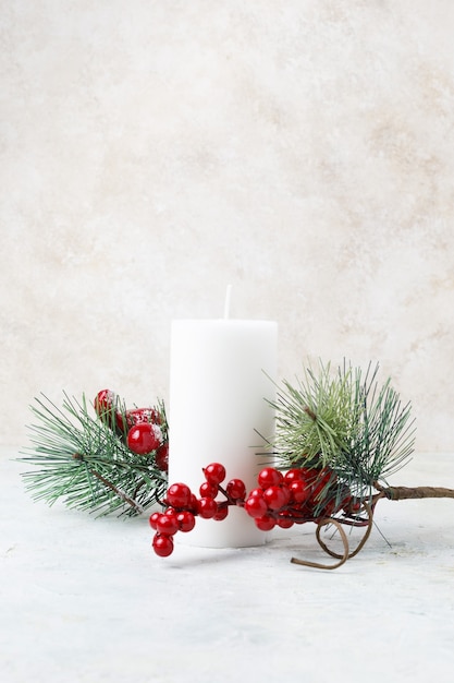 Free photo vertical shot of a white candle surrounded by christmas hollies and leaves on a white marble surface