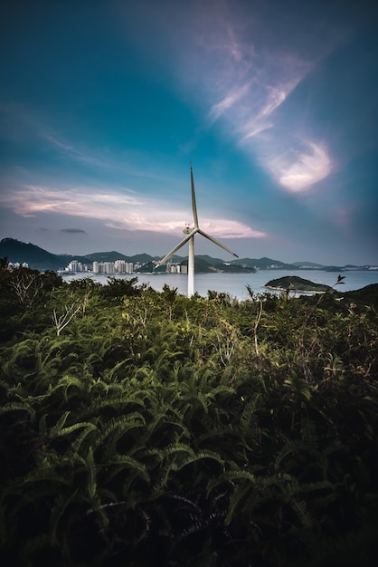 Free Photo vertical shot of a wind turbine in a field with the sea in the background