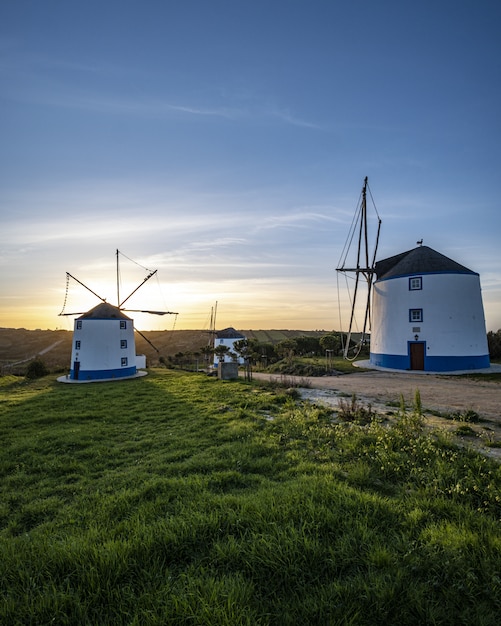 Free photo vertical shot of windmills with a sunrise in a clear blue sky in the background