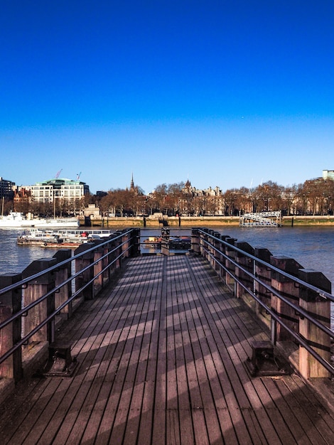 Free photo vertical shot of a wooden dock leading to the river with the city