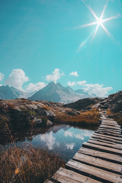 Vertical shot of a wooden passage over a reflective small lake and a mountain range on the horizon