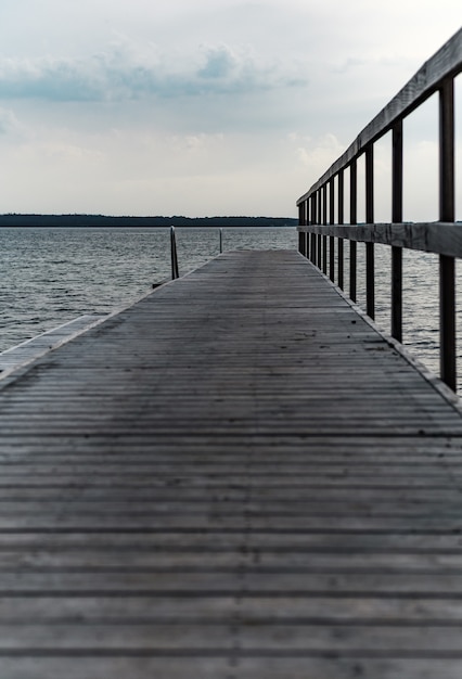 Free Photo vertical shot of a wooden pier at the cpast of the beautiful see under a cloudy sky