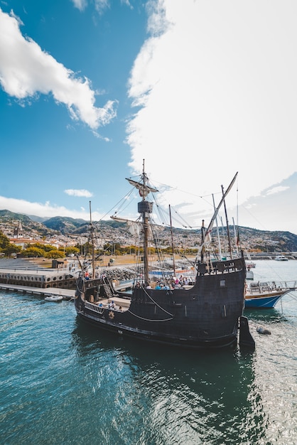 Free photo vertical shot of a wooden ship on the water near the dock in funchal, madeira, portugal.