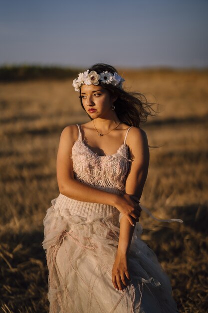 Vertical shot of a young caucasian female in white dress and white flower wreath posing in a field