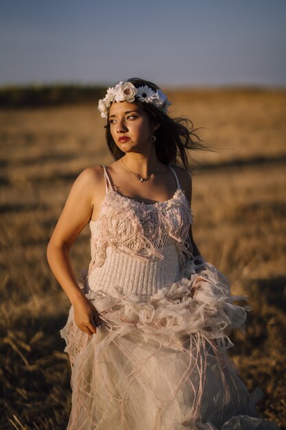 Vertical shot of a young caucasian female in white dress and white flower wreath posing in a field