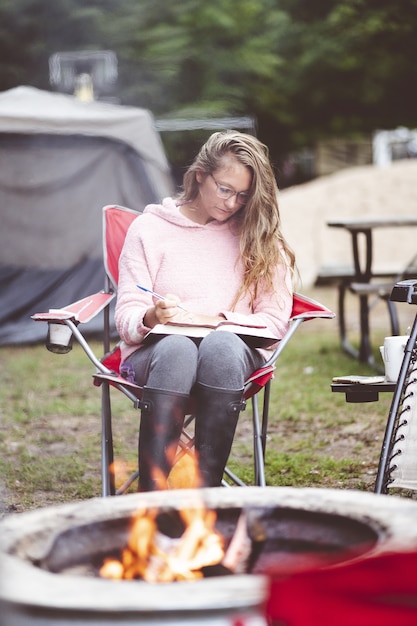 Free Photo vertical shot of a young female studying outdoors in front of a fire