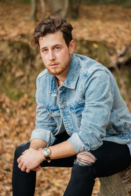 Vertical shot of a young handsome guy in an autumn park