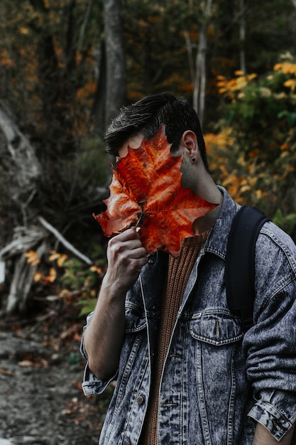 Free photo vertical shot of a young male covering his entire face with a large golden autumn leaf