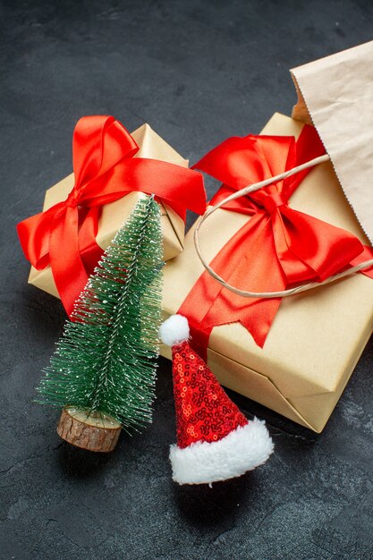 Vertical view of beautiful gifts with red ribbon and christmas tree santa claus hat on a dark table