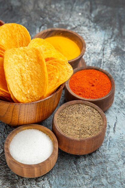 Vertical view of crispy chips on wooden cutting board served with different spices mayonnaise and ketchup on gray table