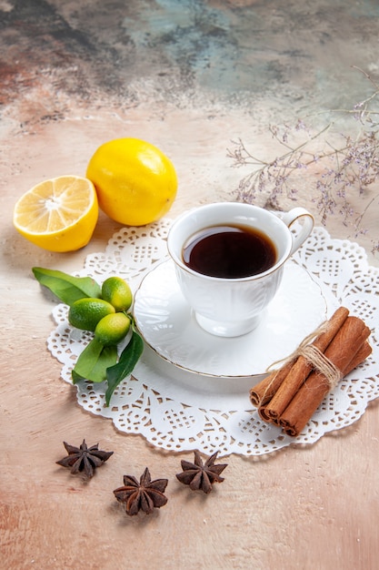 Vertical view of a cup of black tea on decorated napkin with fruits cinnamon on colourful table