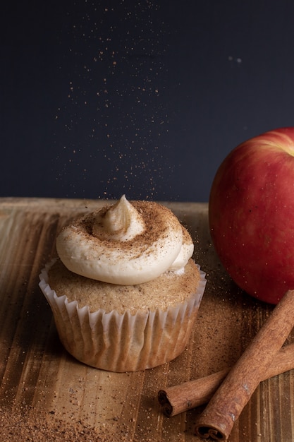 Free photo vertical view of a cupcake with frosting while sprinkling a coffee powder on top