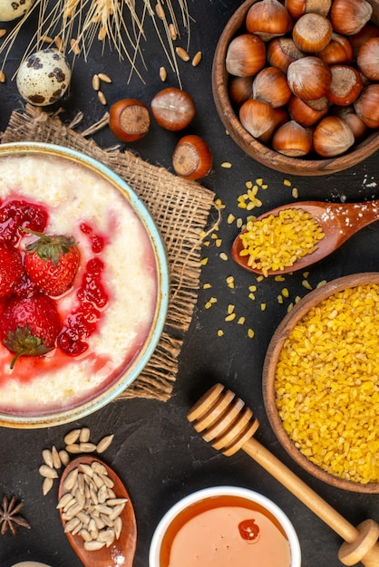 Vertical view of delicious breakfast served with strawberries jam in a bowl and honey hazelnuts spoons on dark color background