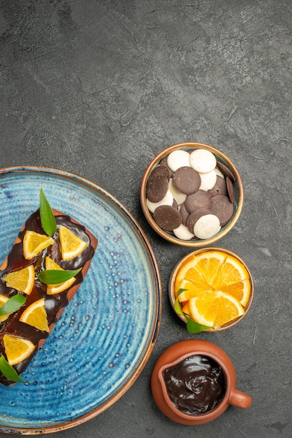 Free Photo vertical view of delicious cake decorated with lemon and chocolate with other cookies on dark table